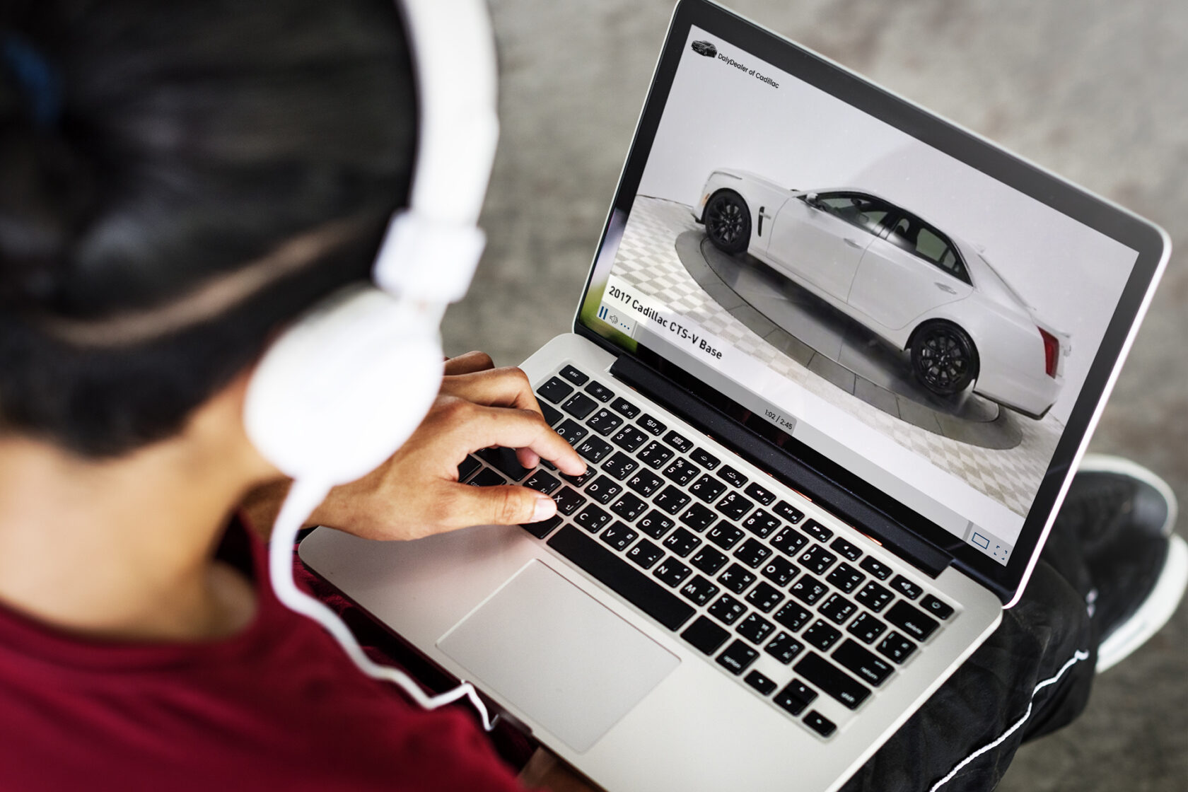 Person with headphones looking at a car on a laptop.